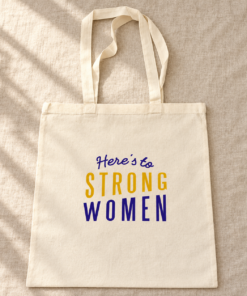 Cream canvas Here’s to Strong Women tote bag with purple and mustard-yellow lettering